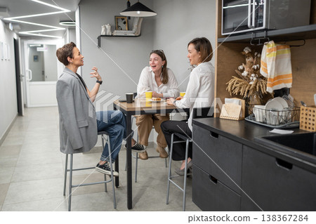 Colleagues laughing and talking around kitchen counter in modern company wth drinks and snacks. Laughing, talking, kitchen, drinks, teamwork, company. Colleagues laughing and talking around kitchen counter in modern company wth drinks and snacks. Laughing, talking, kitchen, drinks, teamwork, company. 138367284