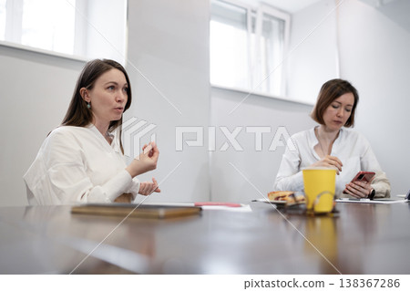 Two women talking side by side at desk with coffee and orange juice during work discussion. Talking, desk, juice, coffee, work, discussion, women. Two women talking side by side at desk with coffee and orange juice during work discussion. Talking, desk, juice, coffee, work, discussion, women. 138367286
