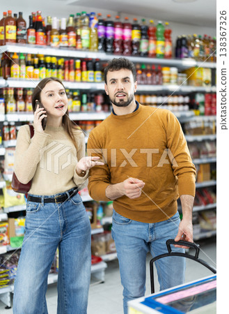 Young couple shopping for groceries woman talks on phone Young couple shopping for groceries woman talks on phone 138367326