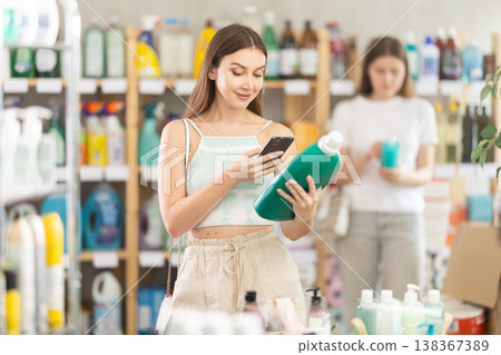 Woman scans QR code on label of detergent using her smartphone, while in background shoppers browse products Woman scans QR code on label of detergent using her smartphone, while in background shoppers browse products 138367389