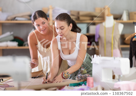 Two female dressmakers drawing patterns on paper Two female dressmakers drawing patterns on paper 138367502