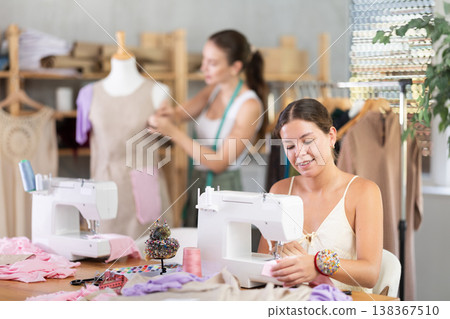 Woman seamstress operating by sewing machine. Assistant work with mannequin in background 138367510