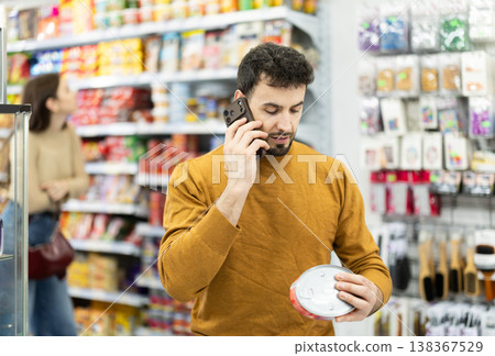 In store, man examines tin can product and talks on phone, advises on purchase. 138367529