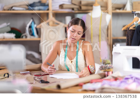 Young tailoress engaged in paperwork in sewing workshop 138367538