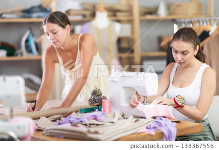 fashion designer draws patterns of dresses next to a seamstress 138367556