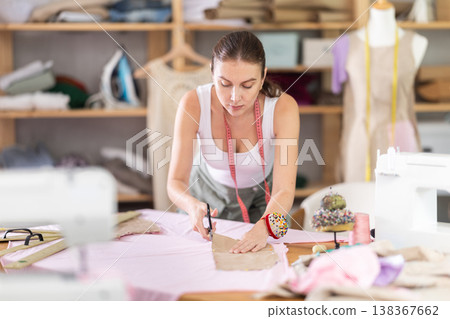 Young female dressmaker cutting textile in sewing workshop 138367662