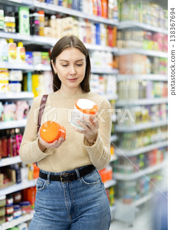 Positive woman buyers chooses shampoo or shower gel in household chemicals store Positive woman buyers chooses shampoo or shower gel in household chemicals store 138367694