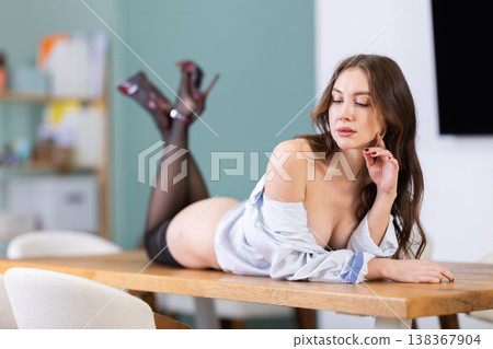 Half-naked topless girl in underwear string pants and white shirt poses and lies on table Half-naked topless girl in underwear string pants and white shirt poses and lies on table 138367904