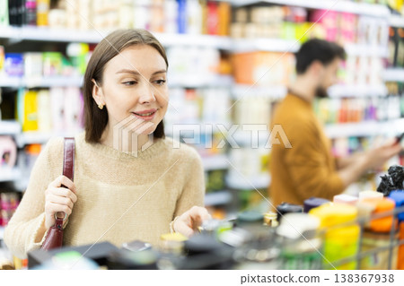 Positive woman buyers chooses shampoo or shower gel in household chemicals store Positive woman buyers chooses shampoo or shower gel in household chemicals store 138367938