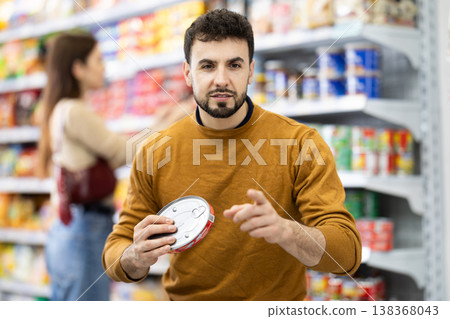 Man in supermarket search and select product tin can Man in supermarket search and select product tin can 138368043