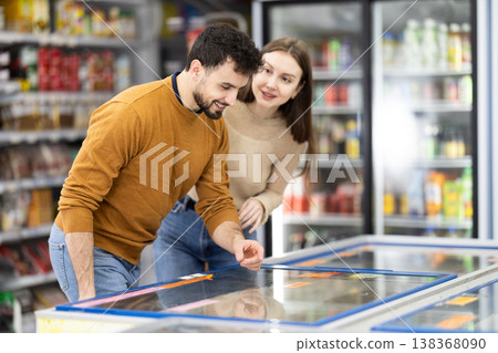 Couple spends time in store, looking for necessary goods and get out from refrigerator Couple spends time in store, looking for necessary goods and get out from refrigerator 138368090