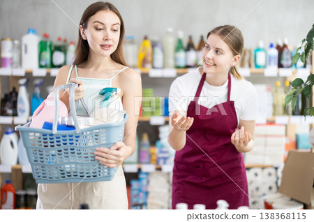 Female salesperson and customer with shopping basket choosing goods together in supermarket Female salesperson and customer with shopping basket choosing goods together in supermarket 138368115