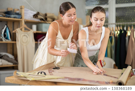 Two female dressmakers drawing patterns on paper Two female dressmakers drawing patterns on paper 138368189