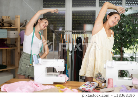 Female dressmakers doing a warm-up in the workshop in summer Female dressmakers doing a warm-up in the workshop in summer 138368190