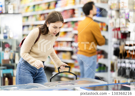 Woman spends time in store, looking for necessary goods and get out from refrigerator Woman spends time in store, looking for necessary goods and get out from refrigerator 138368216