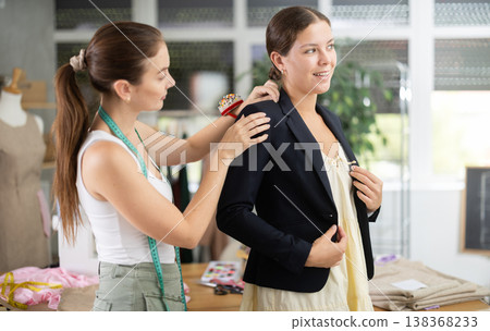 Young tailoress trying ready jacket on female client Young tailoress trying ready jacket on female client 138368233
