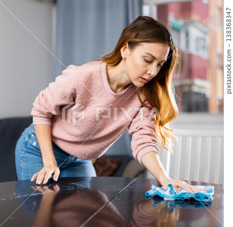 Young woman wipes the table with a damp rag 138368347