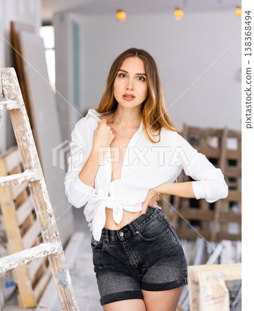Young brown-haired woman in shorts and unbuttoned blouse standing in apartment during overhaul 138368494