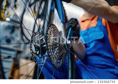 Expert technician carefully adjusting gear system on bicycle in cluttered workspace 138368734