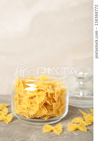 Raw farfalle pasta on glass jar on grey background. Vertical photo Raw farfalle pasta on glass jar on grey background. Vertical photo 138368772