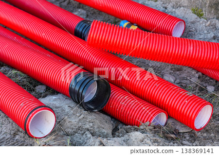 Red corrugated plastic pipes on ground for drainage or cable conduit installation at construction Red corrugated plastic pipes on ground for drainage or cable conduit installation at construction 138369141