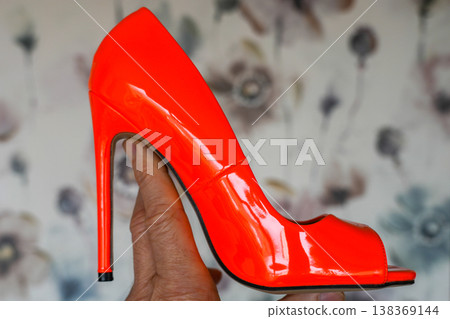 Bright red high heel shoe held in hand glossy patent leather fashion statement footwear Bright red high heel shoe held in hand glossy patent leather fashion statement footwear 138369144