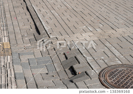 Damaged pavement with displaced paving stones and manhole cover on urban sidewalk surface 138369168