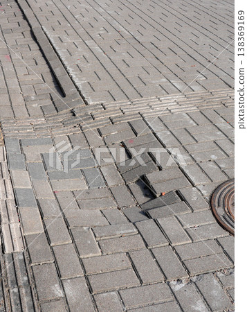 Uneven sidewalk with broken paving stones and manhole cover showing urban surface damage detail 138369169