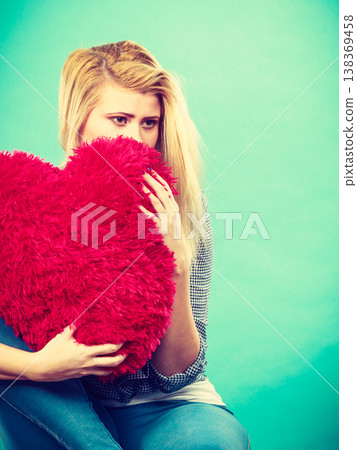 Sad woman holding red pillow in heart shape Sad woman holding red pillow in heart shape 138369458