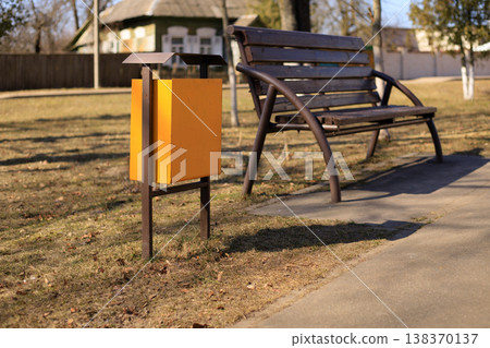 Yellow metal trash can in a public city park near a walking path. Yellow metal trash can in a public city park near a walking path. 138370137