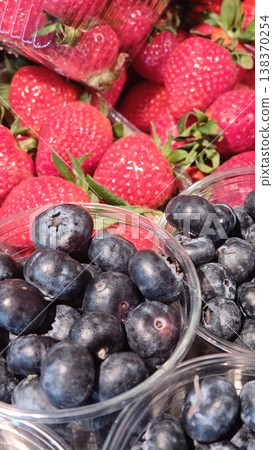 Fresh strawberries and blueberries displayed in clear plastic containers at a market, showcasing vibrant colors and natural textures of the fruits 138370254
