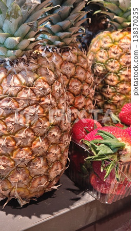 Fresh pineapples and strawberries displayed together on a market shelf, showcasing vibrant colors and textures of tropical fruits in a grocery setting 138370255