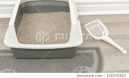 Odor-free litter box with gray sand and white scoop on a mat, placed on a light wooden floor in a clean indoor setting Odor-free litter box with gray sand and white scoop on a mat, placed on a light wooden floor in a clean indoor setting 138370367