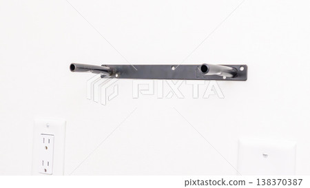 Black metal shelf bracket with level markings attached to white wall near electrical outlet. Home improvement, installed hardware, DIY shelf preparation, wall fixture. 138370387