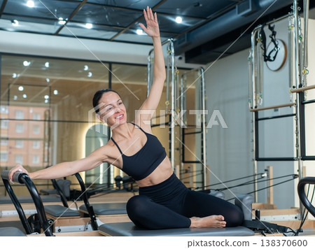 Caucasian woman doing side bends on reformer machine. Caucasian woman doing side bends on reformer machine. 138370600