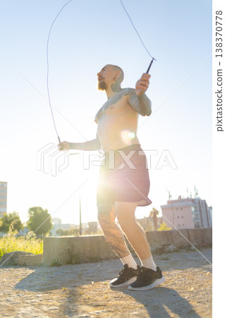 Tattooed man skipping rope exercising outdoors Tattooed man skipping rope exercising outdoors 138370778