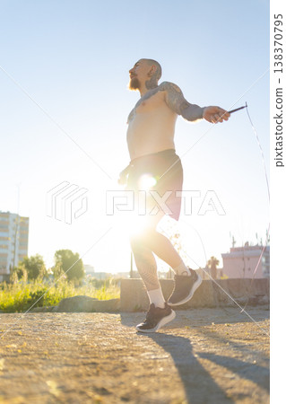 Tattooed man skipping rope during intense outdoor workout Tattooed man skipping rope during intense outdoor workout 138370795