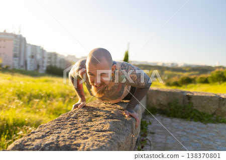 Tattooed man training outdoors doing upper body workout 138370801