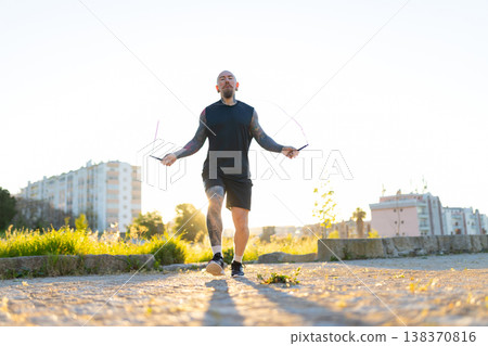 Tattooed man exercising outdoors jumping rope at sunset 138370816
