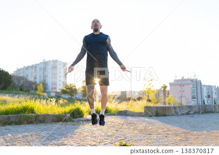 Tattooed man actively jumping rope during outdoor workout 138370817