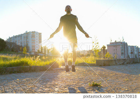 Determined man jumping rope outdoors at sunset 138370818