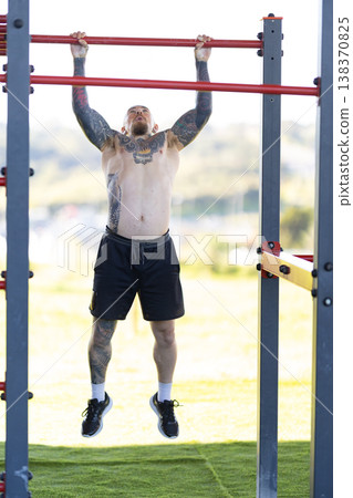 Man performing pull-up exercise at outdoor urban gym 138370825