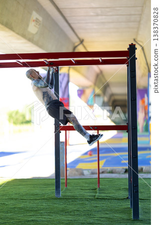 Tattooed man training calisthenics on monkey bars outdoors Tattooed man training calisthenics on monkey bars outdoors 138370828
