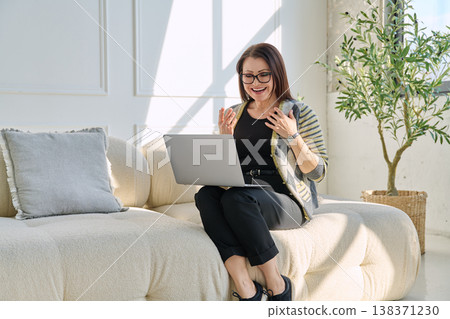 Middle aged woman sitting at home on sofa using laptop for video call, chat 138371230