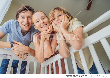 Parents and older brother looking into baby crib from infant point of view. Family smiling down at newborn with love and care. Sibling bonding, parenthood, childhood memory and connection concept 138371632