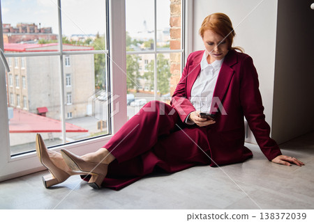 Businesswoman with fiery hair analyzing updates over cityscape view 138372039