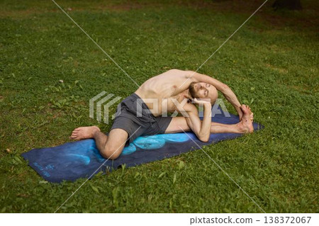 Shirtless man lying on blue mat calmly exercising and breathing in park Shirtless man lying on blue mat calmly exercising and breathing in park 138372067
