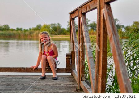 Joyful young girl laughing on a wooden dock by the water during golden hour Joyful young girl laughing on a wooden dock by the water during golden hour 138372621