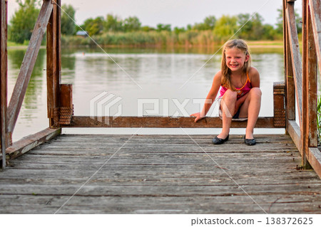 Young girl with a big smile sitting on a wooden dock by the lake 138372625