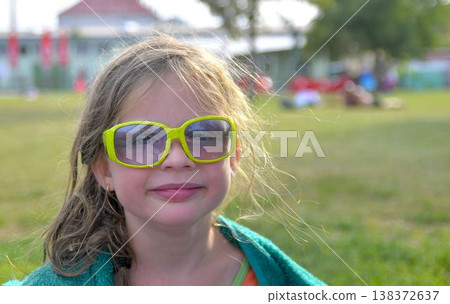 A cute little girl with sunglasses at the swimming pool. A small smiling girl in a pool towel at the swimming pool. The concept of summer, summer vacations, rest, and relaxation. A cute little girl with sunglasses at the swimming pool. A small smiling girl in a pool towel at the swimming pool. The concept of summer, summer vacations, rest, and relaxation. 138372637